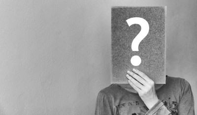 Paper with question mark being held in front of a face