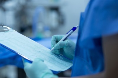 Nurse in surgical scrubs writing on a clipboard
